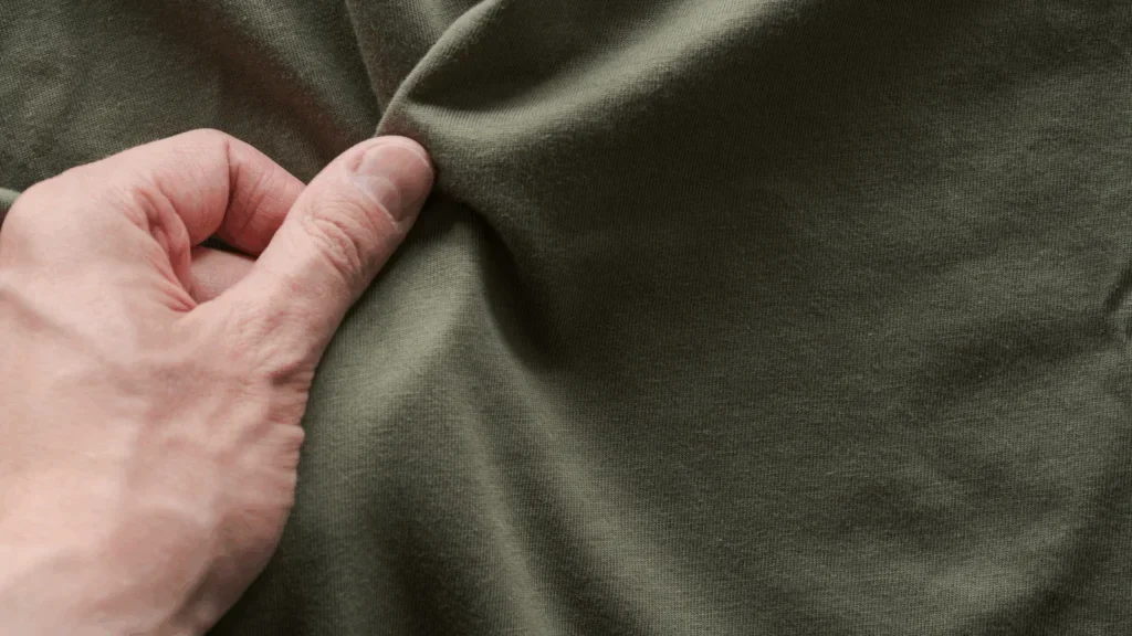 A hand inspecting the texture of dark green fabric.